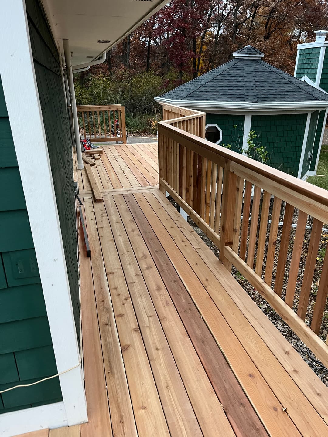 Wooden deck extension showcasing smooth cedar boards and green accents of the house.