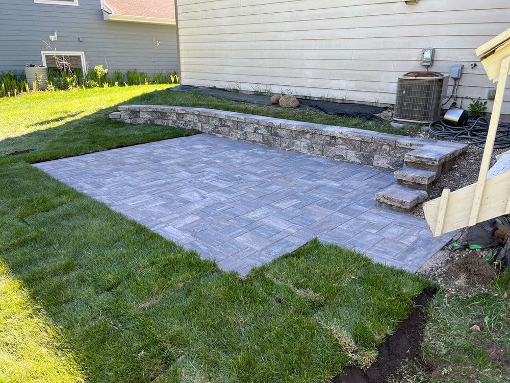 Paved patio area with stone steps and landscaped grass in a residential backyard.