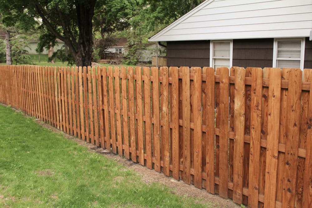 Wooden fence in a residential backyard with a house and green lawn in the background.