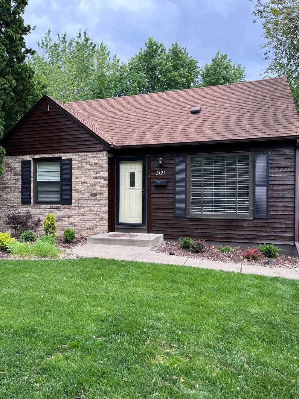 Charming brown house with a brick exterior, green lawn, and shrubs in front.